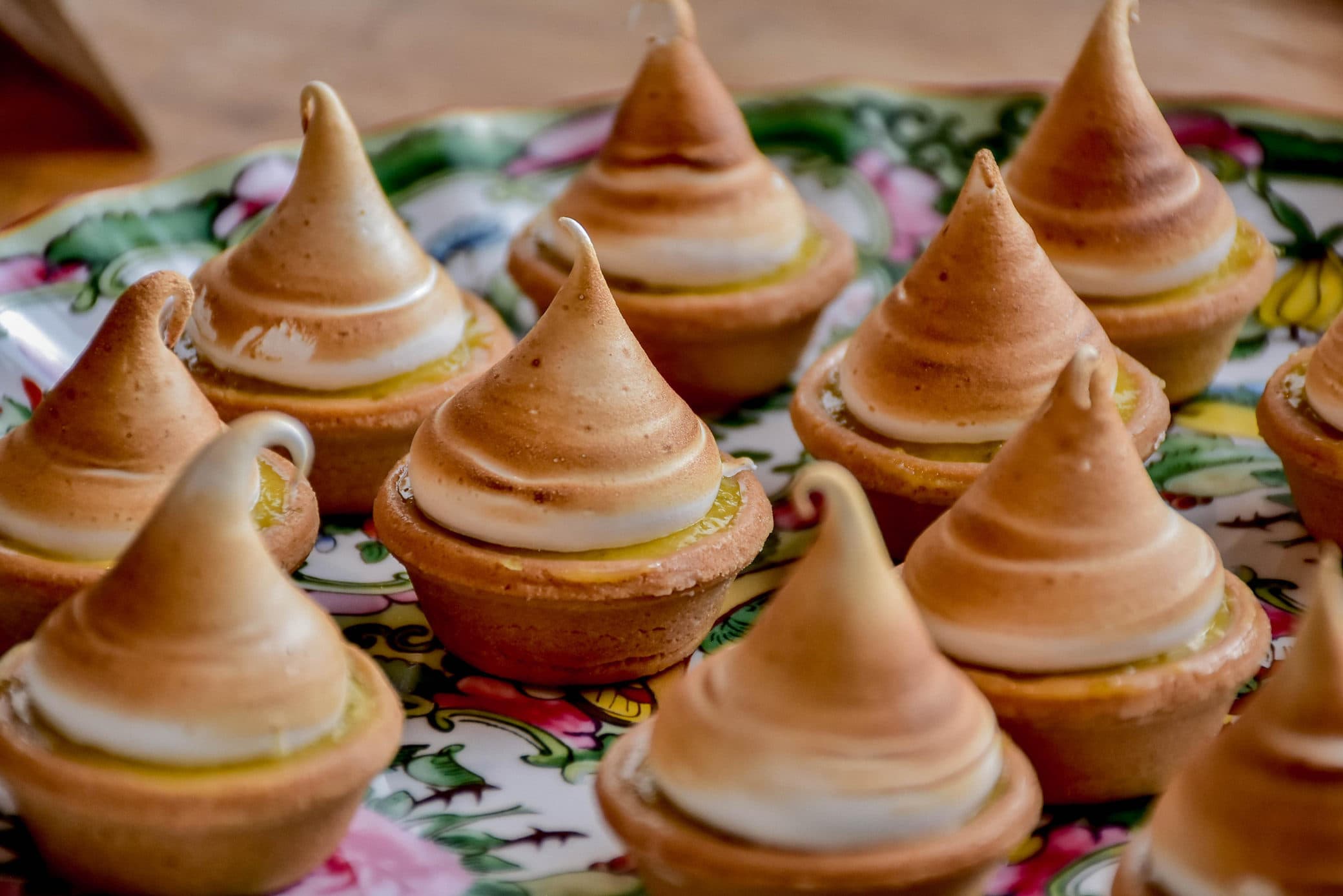 Tartaletas de limón con merengue dorado sobre un plato de porcelana floral